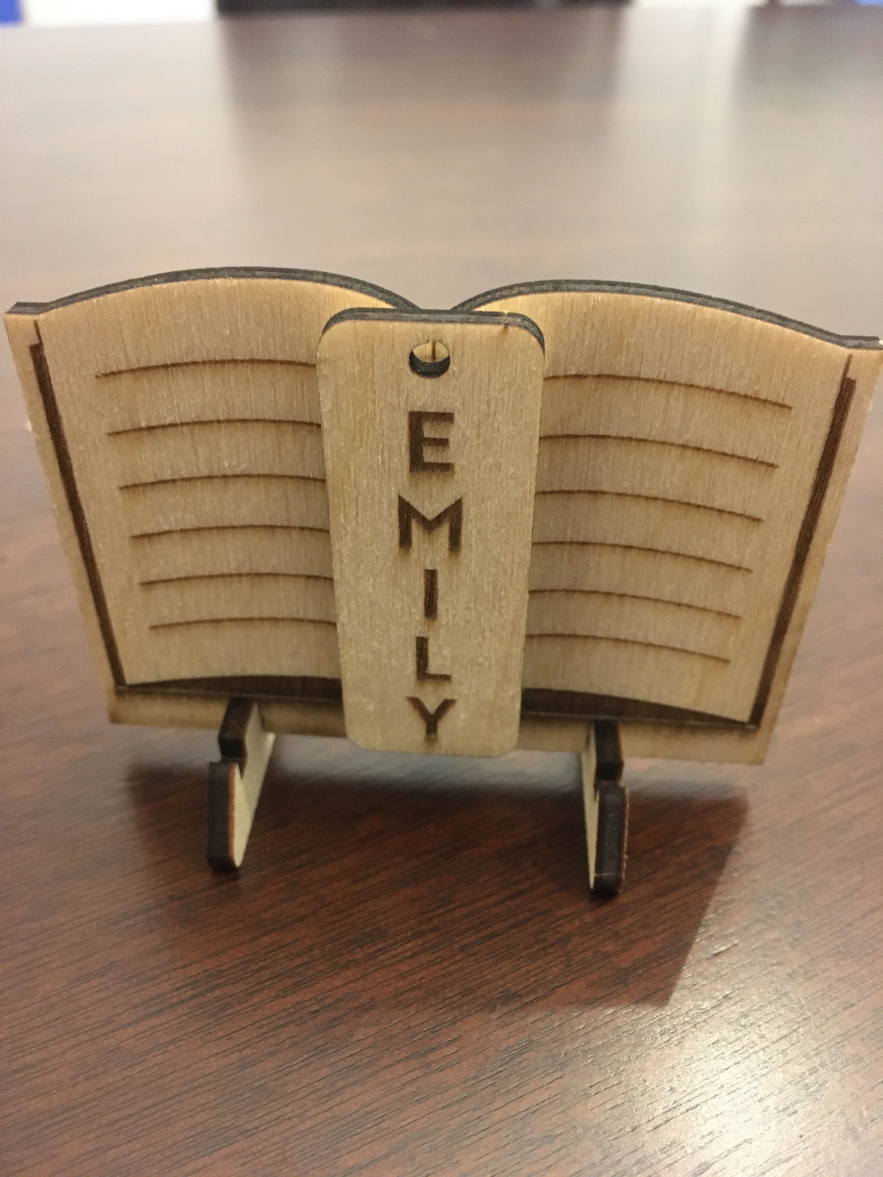 laser cut wood nametag and stand, nametag reads Emily, stand looks like an open book